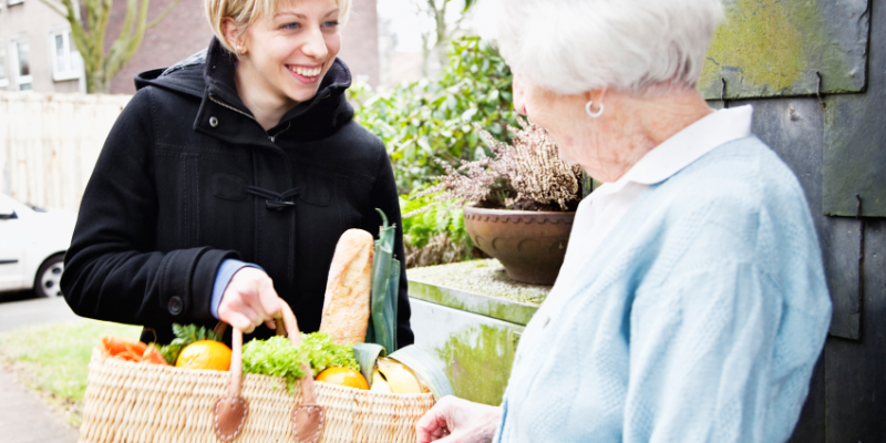 Woman giving shopping basket of helathy food to older woman