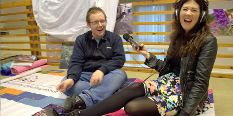 Person, smiling, holding microphone to interview