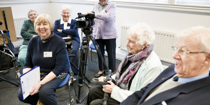 picture of older people smiling holding a camera and recording equipment